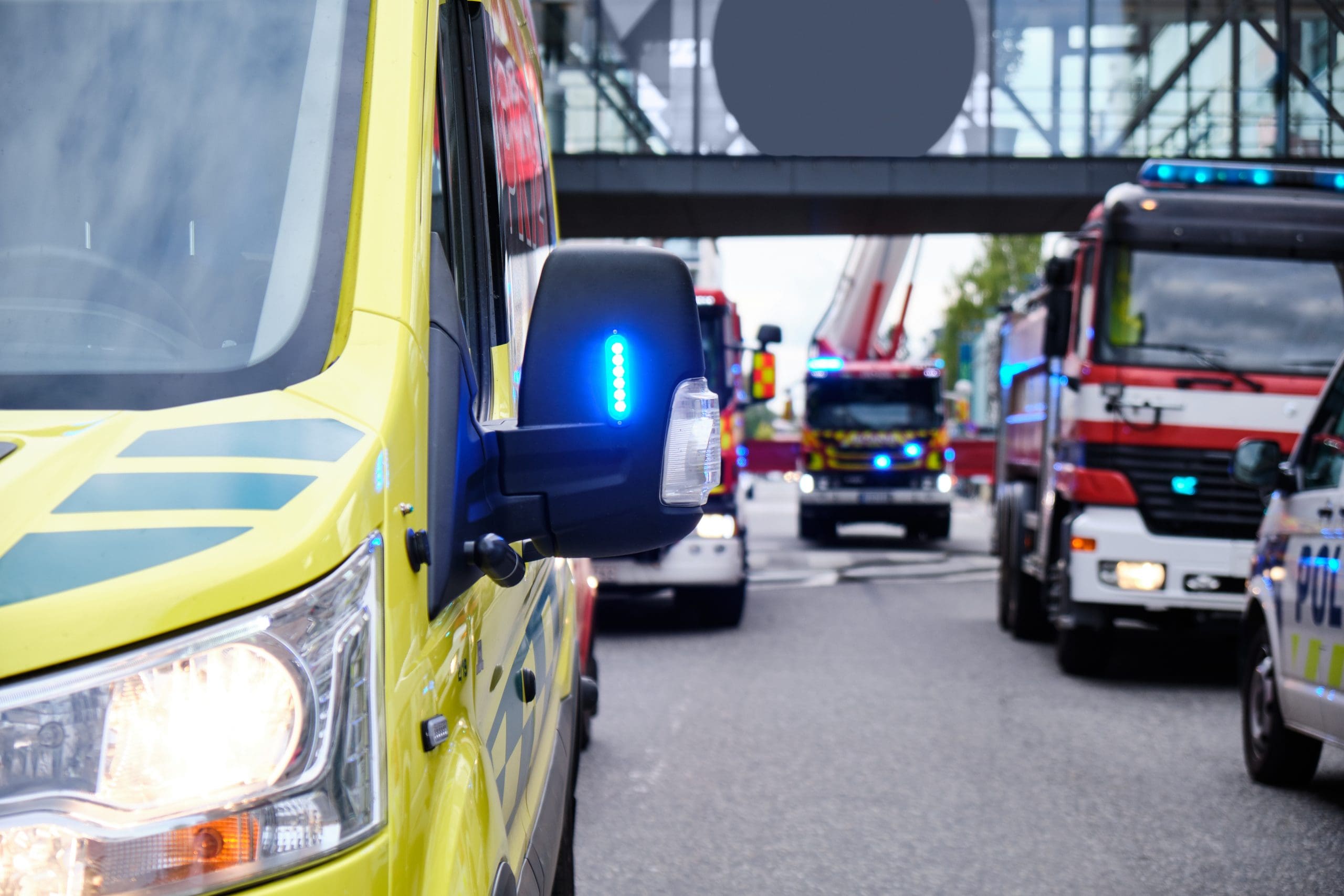 Ambulance car, fire engines and a police car with blue lights near the shopping mall.